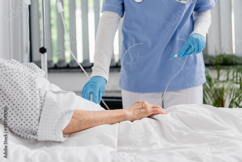 Cropped view of nurse holding catheter near senior woman on hospital bed