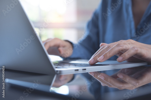 Closeup image of a business woman's hands working and typing on laptop keyboard on glass table with reflection