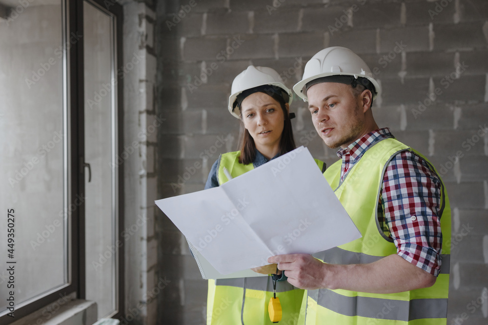 two engineers woman and man in white helmets and yellow safety vests at the construction site discuss the work plan, design engineers or designers work at the construction site, the technical work of two engineers woman and man in white helmets and yellow safety vests at the construction site discuss the work plan, design engineers or designers work at the construction site, the technical work of