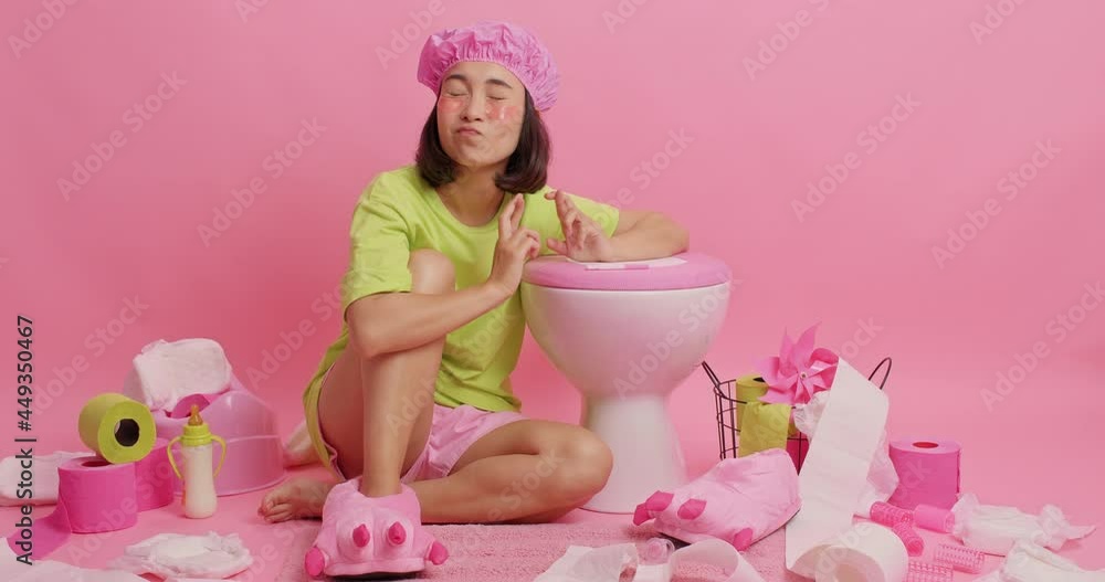 Overjoyed Asian woman waits for pregnancy result tests clenches fist from joy feels very happy and exclaims enjoys moment poses near toilet bowl in restroom wears bathhat applies beauty patches Overjoyed Asian woman waits for pregnancy result tests clenches fist from joy feels very happy and exclaims enjoys moment poses near toilet bowl in restroom wears bathhat applies beauty patches
