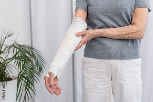 Photos Cropped view of senior woman touching arm in plaster bandage in clinic