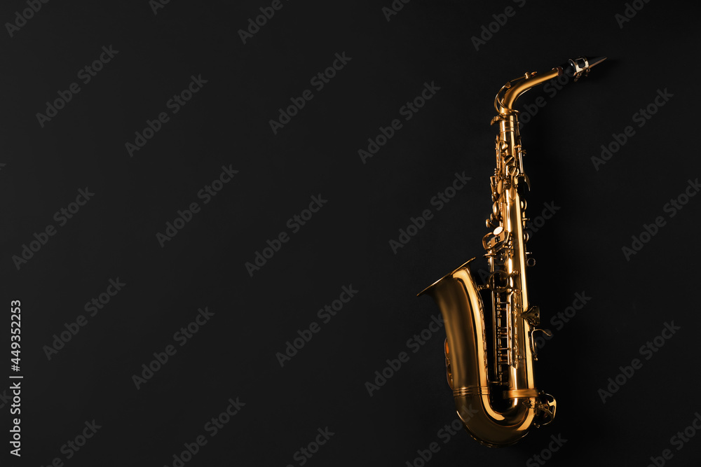 Naklejka premium Beautiful saxophone on black background, top view. Space for text