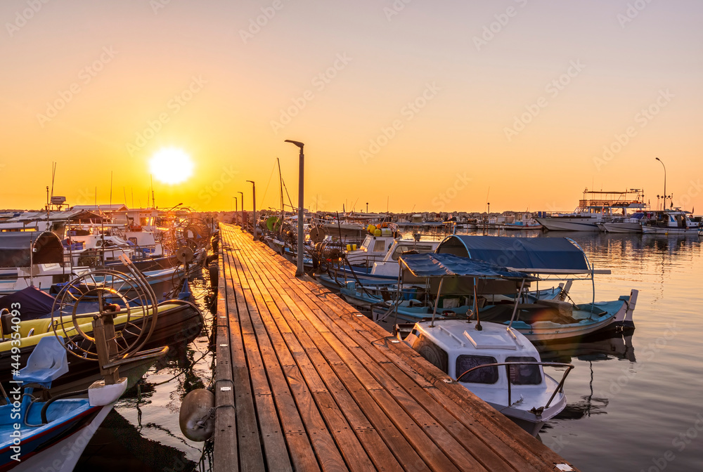 Obraz premium tranquil sunrise in fishing docks with sunny pier , leading far to sea and golden sun with sailing boats moored around