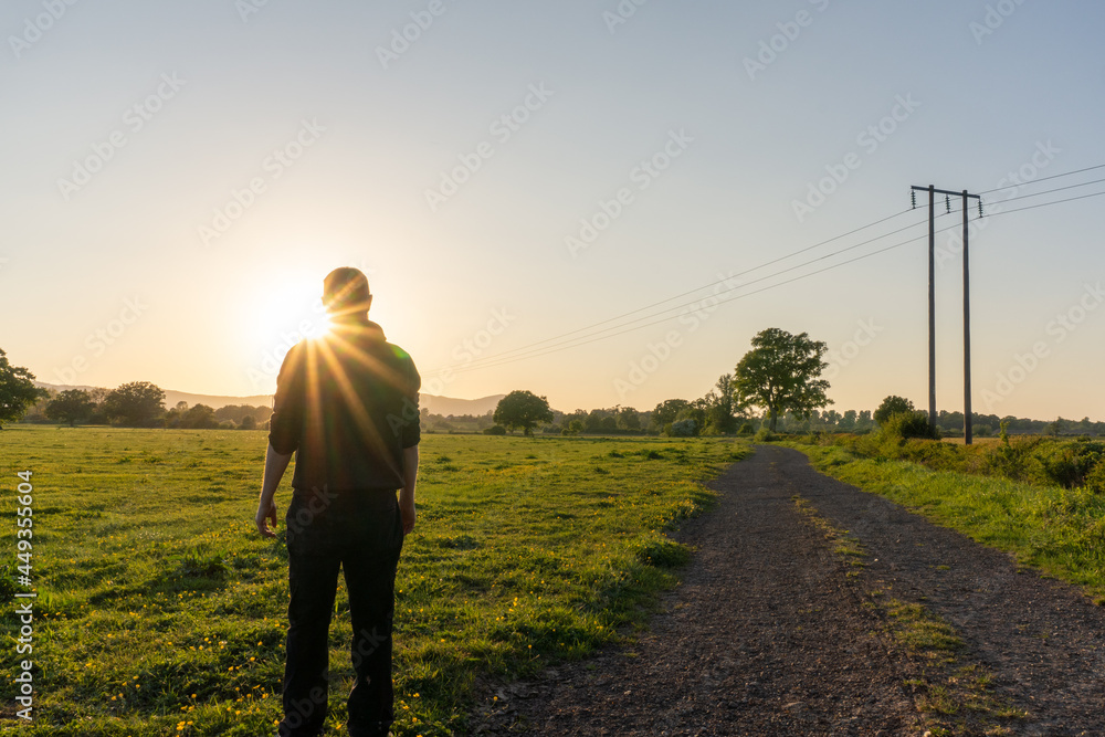 A man looking at the sunset. With sun flare. In the countryside on a spring evening.