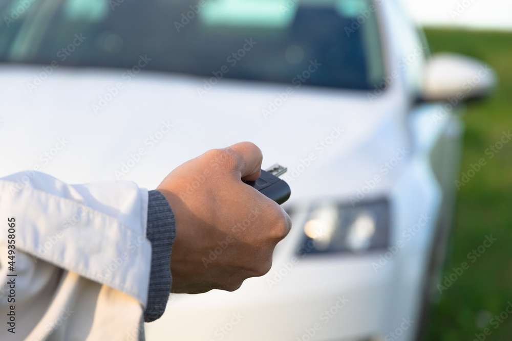 A woman's hand holds the key to a new white car and opens it on a bright sunny summer day against a background of green grass. Selective focus. Close-up