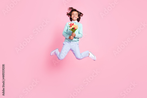 Photo of cheerful romantic boy jump hold flower bouquet wear teal shirt isolated pink color background
