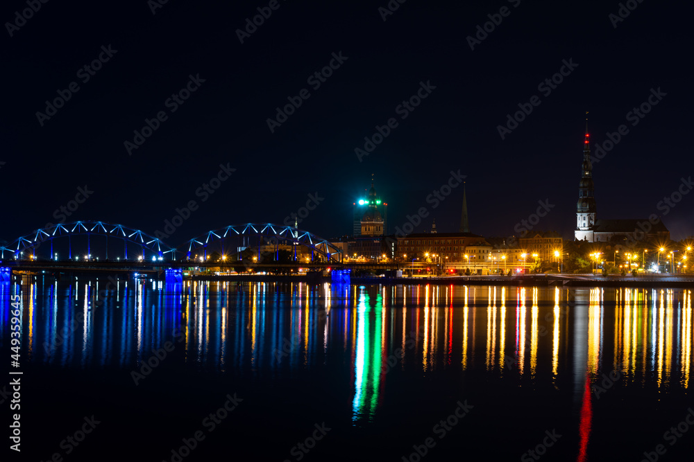 View of Riga (Latvia) in the evening. Old buildings and a railway bridge are illuminated and reflect in the Daugava river.