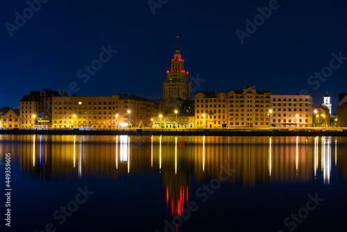 Summer dawn over the illuminated old buildings of the Moscow district and the quiet waters of the Daugava river in Riga  Latvia. Tower of the Science Academy building on the background.