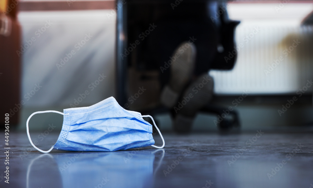 Medical mask on the floor of an office, abandoned with somebody working in the background
