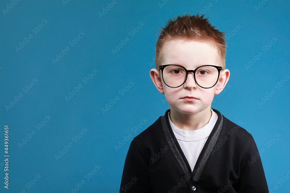 Back to school. portrait of sad little clever school boy in glasses look at the camera, isolated on blue background Back to school. portrait of sad little clever school boy in glasses look at the camera, isolated on blue background