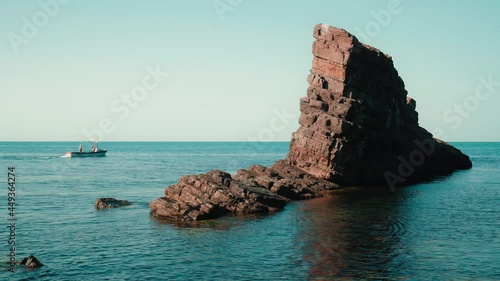 Mid angle view of natural landmark The stone ships near Sinemorets, Bulgaria. Colorful landscape of rocks in calm blue sea water during a sunny day. Waves crashing on coast and fishing boat passing by