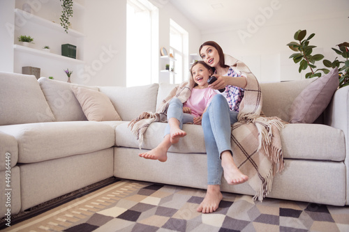 Full length photo of cheerful happy positive pretty sisters siblings watch tv sit sofa indoors inside house home
