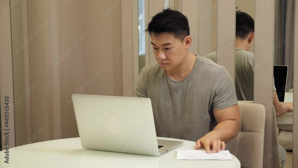Serious asian male accountant sitting in home office do work distantly managing company budget, count financial plan use calculator calculates expenses typing writing digits results into application. Serious asian male accountant sitting in home office do work distantly managing company budget, count financial plan use calculator calculates expenses typing writing digits results into application.
