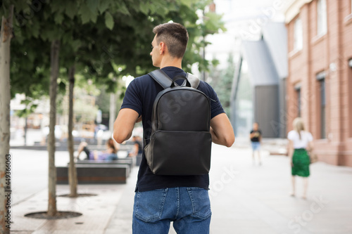 Rear view man walking in city with black leather backpack on his shoulders photo
