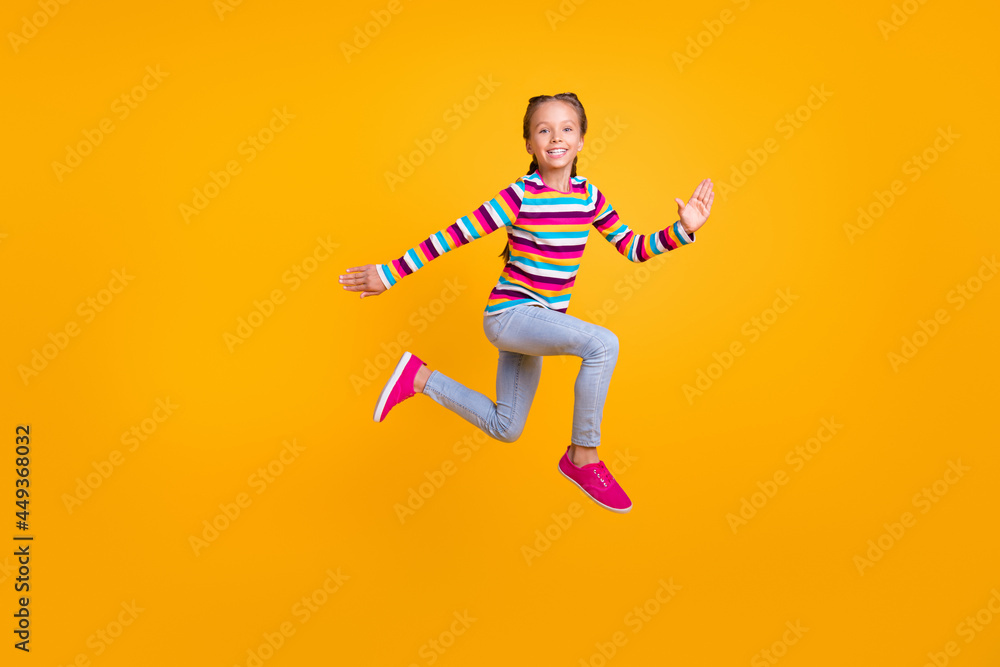 Photo of carefree runner sporty girl jump hurry fast wear striped shirt jeans shoes isolated yellow color background