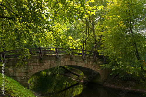 Fototapeta Naklejka Na Ścianę i Meble -  Vintage beautiful stone bridge among large green trees in the city park
