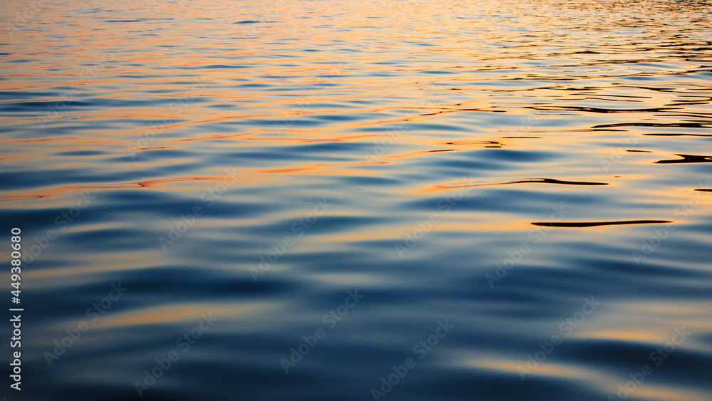 Fototapeta premium Reflection of sunset in waves of river, selective focus. Water surface with waves in the evening. Ripple water texture.