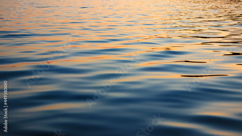 Reflection of sunset in waves of river, selective focus. Water surface with waves in the evening. Ripple water texture.