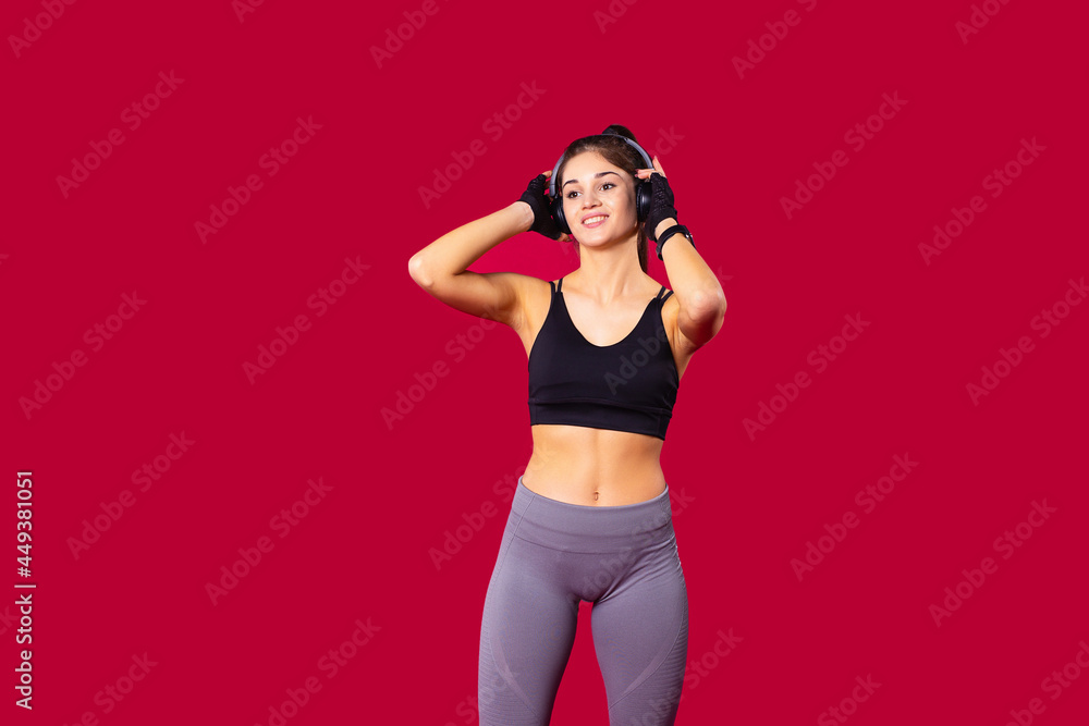 The girl with athletic body standing in front of the camera in sports clothes, holding the headphones with her hands listening the music. The girl with athletic body standing in front of the camera in sports clothes, holding the headphones with her hands listening the music.