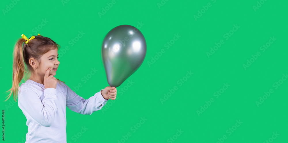 Adorable shiny young girl holding a dark green balloon in front of her and thinking to whom to give it. Adorable shiny young girl holding a dark green balloon in front of her and thinking to whom to give it.
