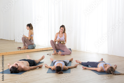 Yoga instructor and group of young sporty people in yoga studio, lying and relaxing on yoga mats during restorative yoga session. Healthy active lifestyle