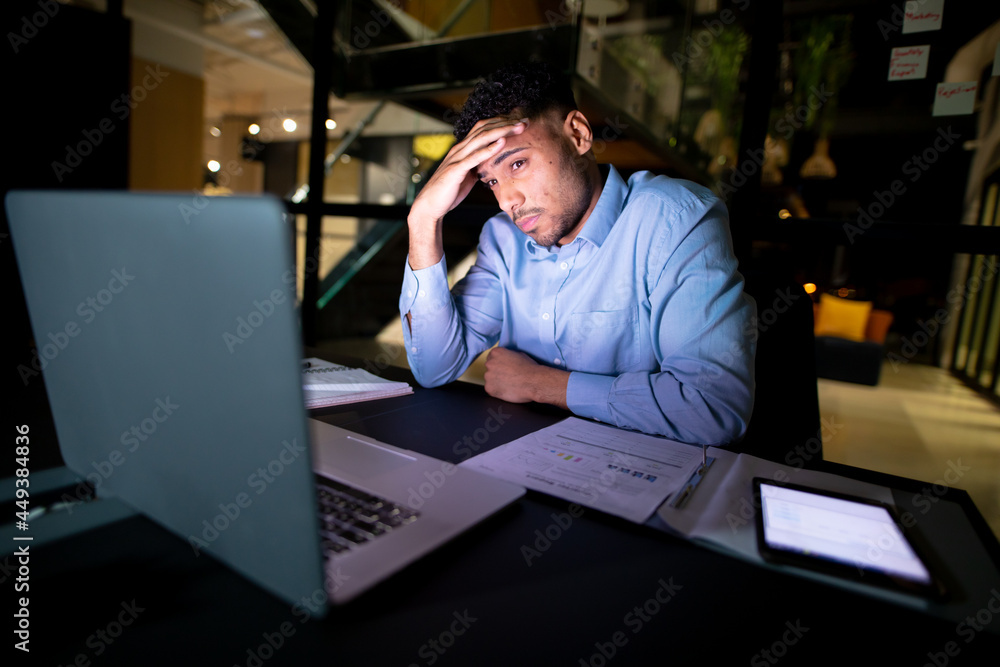 Mixed race businessman working at night, sitting at desk and using laptop Mixed race businessman working at night, sitting at desk and using laptop