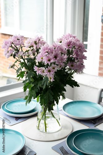 Pink flowers in vase on modern dinning table with blue plates, at home. Chrysanthemum pink flower bouquet. photo
