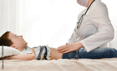 The doctor palpates the baby's stomach, which is filled with laughter in the rays of light from the window.
