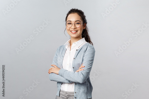 Education, women and lifestyle concept. Attractive asian female entrepreneur, girl tutor smiling satisfied, cross hands chest, pleased help customer with any question, grey background photo