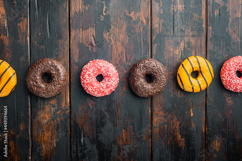 Various decorated donuts set, on old dark wooden table background, top view flat lay with copy space for text