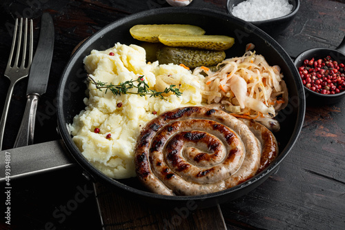 Bavarian fried sausages on sauerkraut in cast iron frying pan, on old dark wooden table background