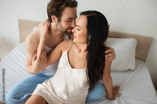 Obraz na plátně bearded man hugging happy girlfriend in camisole dress on bed
