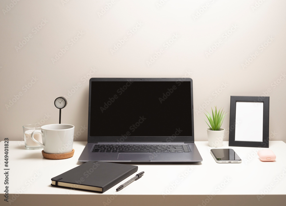 Picture of laptop on a white table with a mug a clock a small bush a notebook a phone a picture frame and a headphone case Picture of laptop on a white table with a mug a clock a small bush a notebook a phone a picture frame and a headphone case