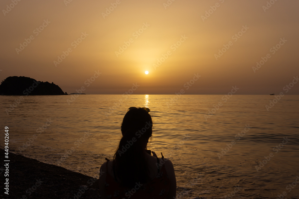 Silhouette of a woman enjoying the sunrise on the beach. Sun rises over the Mediterranean Sea on a lovely summer morning. Selective focus.