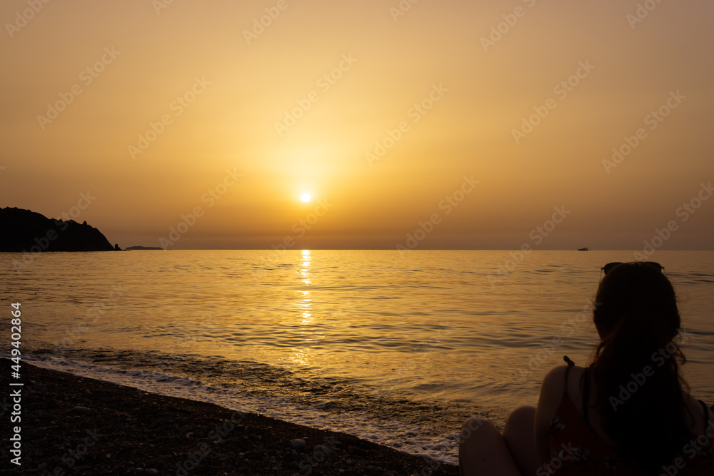 Silhouette of a woman enjoying the sunrise on the beach. Sun rises over the Mediterranean Sea on a lovely summer morning. Selective focus.