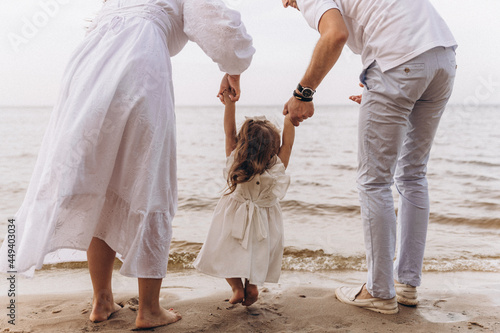 Happy married couple on the seashore holding their daughter by the hands over the sea waves