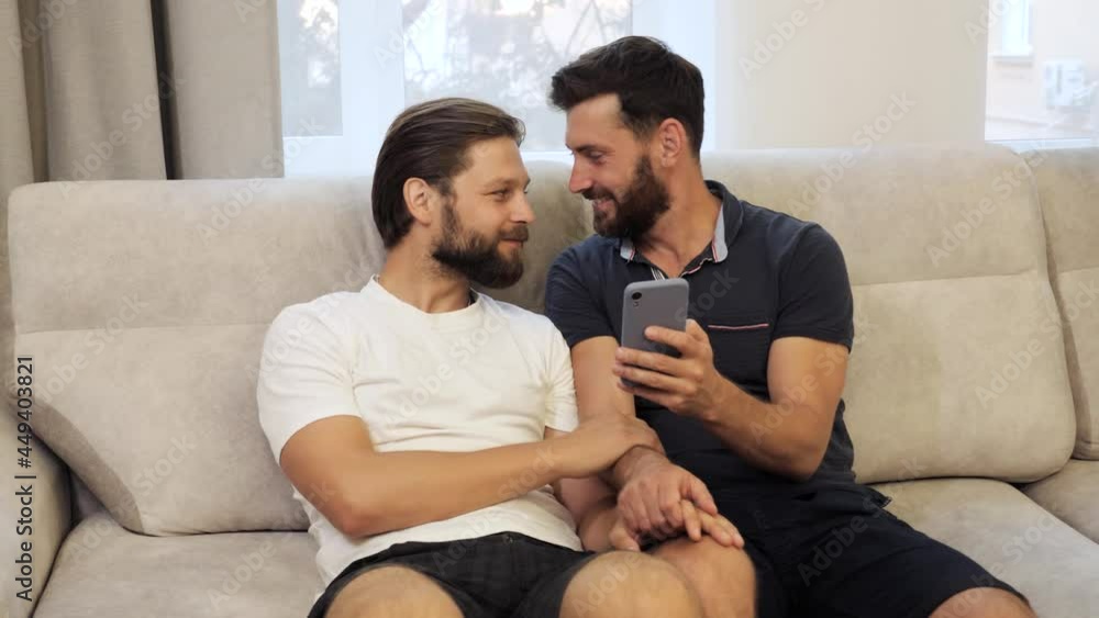Guys Smile and Laugh in Love at Home. Cute Male Homosexual Gay Couple Spend Time Together on the Couch. Men Surfing Social Media on Smartphone. LGBTQI, Pride Event, LGBT Pride Month, Gay Pride Symbol. Guys Smile and Laugh in Love at Home. Cute Male Homosexual Gay Couple Spend Time Together on the Couch. Men Surfing Social Media on Smartphone. LGBTQI, Pride Event, LGBT Pride Month, Gay Pride Symbol.