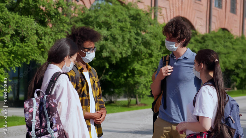 Young diverse students with face mask outside school building talking