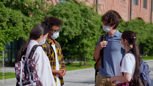 Young diverse students with face mask outside school building talking