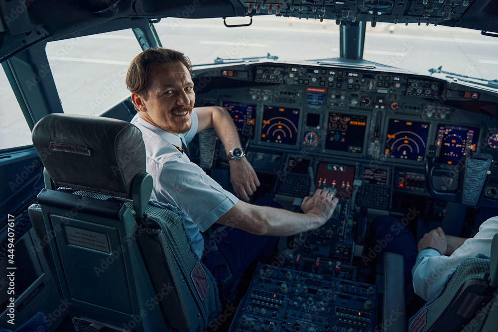 Fototapeta premium Joyful chief pilot posing for the camera in the cockpit