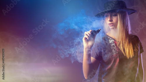 Woman vaper. Girl holds vape device. Stylish girl with electronic cigarette. Woman holds vape device. Woman vaper in clouds of smoke. Concept - smoking nicotine replacement. Alternative to cigarettes © Grispb