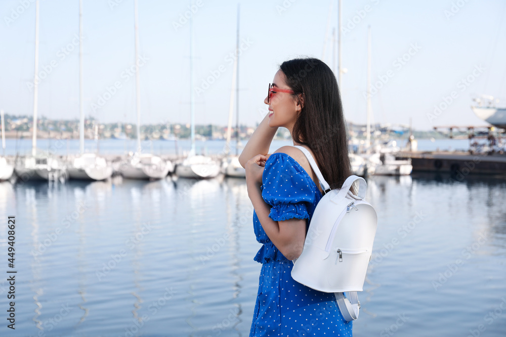 Beautiful young woman with stylish backpack near river