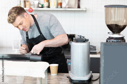 male barista making and pouring coffee to a cup in cafe