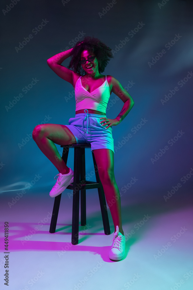 Portrait of African young girl posing isolated on dark blue studio background in pink neon light. Concept of human emotions, facial expression, youth, sales, ad.
