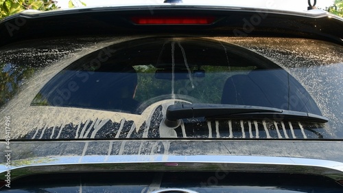 Black car back side and wiper cleaning rear window with sandy drips of dirt due to driving in desert. Dirty car window after off road driving