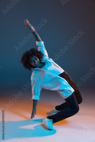 Full-length portrait of African young girl casual clothes, outfit isolated on dark blue studio background in pink neon light. Concept of human emotions, facial expression, youth, sales, ad.