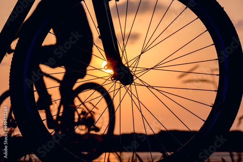 Close-up silhouette of a bike wheel at sunset. The sun shines through the wheel of a bicycle with blurred bicycle rider figure