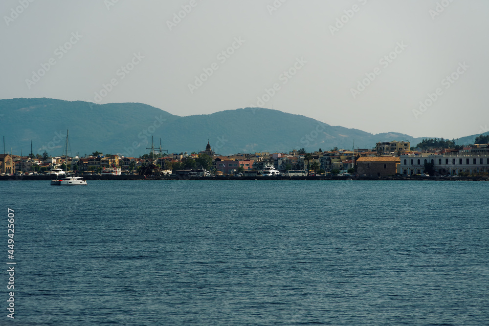 Fototapeta premium Zakynthos, Greece island capital sea view with low rise waterfront buildings. Landscape of houses and stores next to calm sea, with parked tourist buses at the promenade.