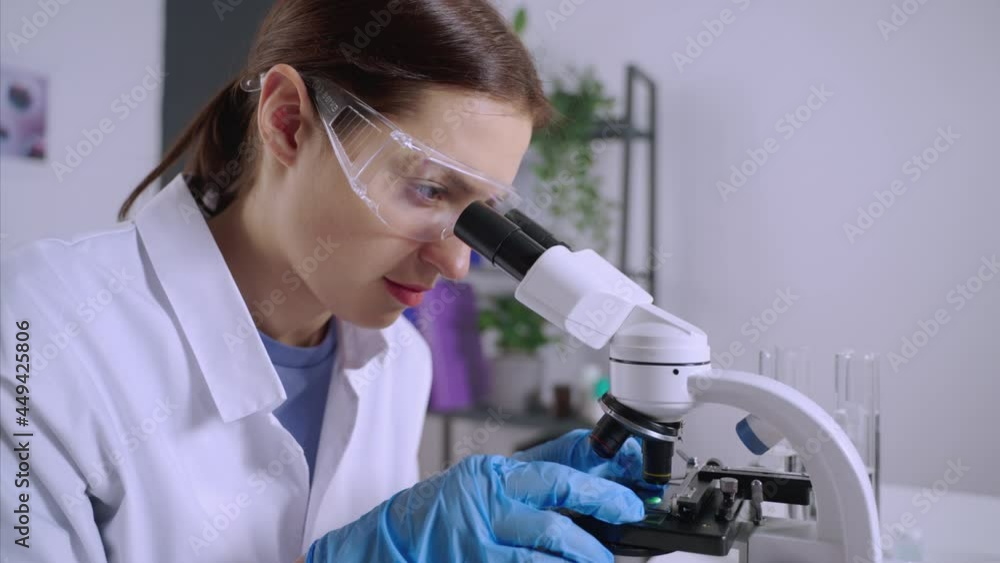 young woman scientist is examining samples under microscope young woman scientist is examining samples under microscope