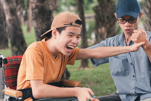 Asian happy disabled teenage boy on wheelchair smiling face with arm muscle strength test with parent, Male style play in teen and lifestyle of diverse family.